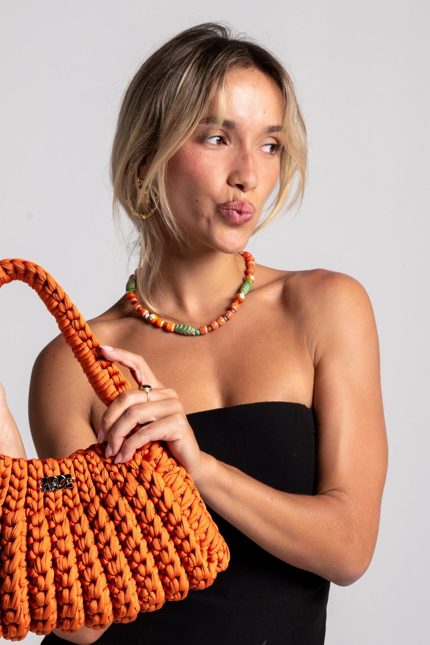Woman holding an orange hand crocheted bag and recycled glass orange and lime necklace against a plain background