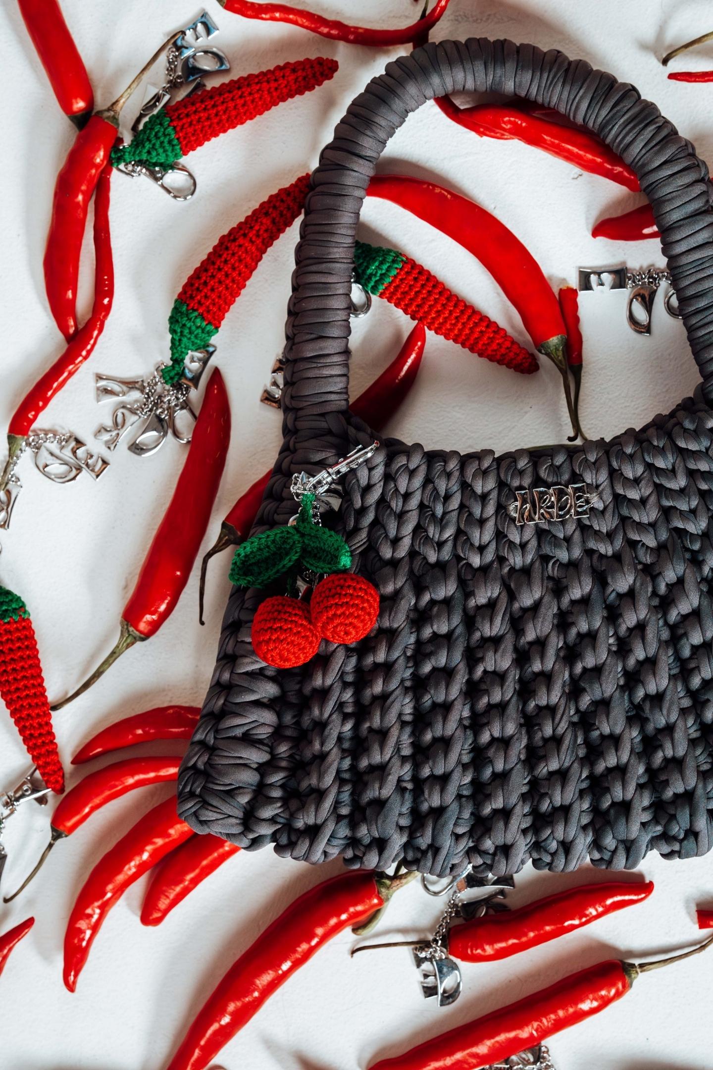 Gray textured handbag with red cherry charm on a white background with red chili peppers.