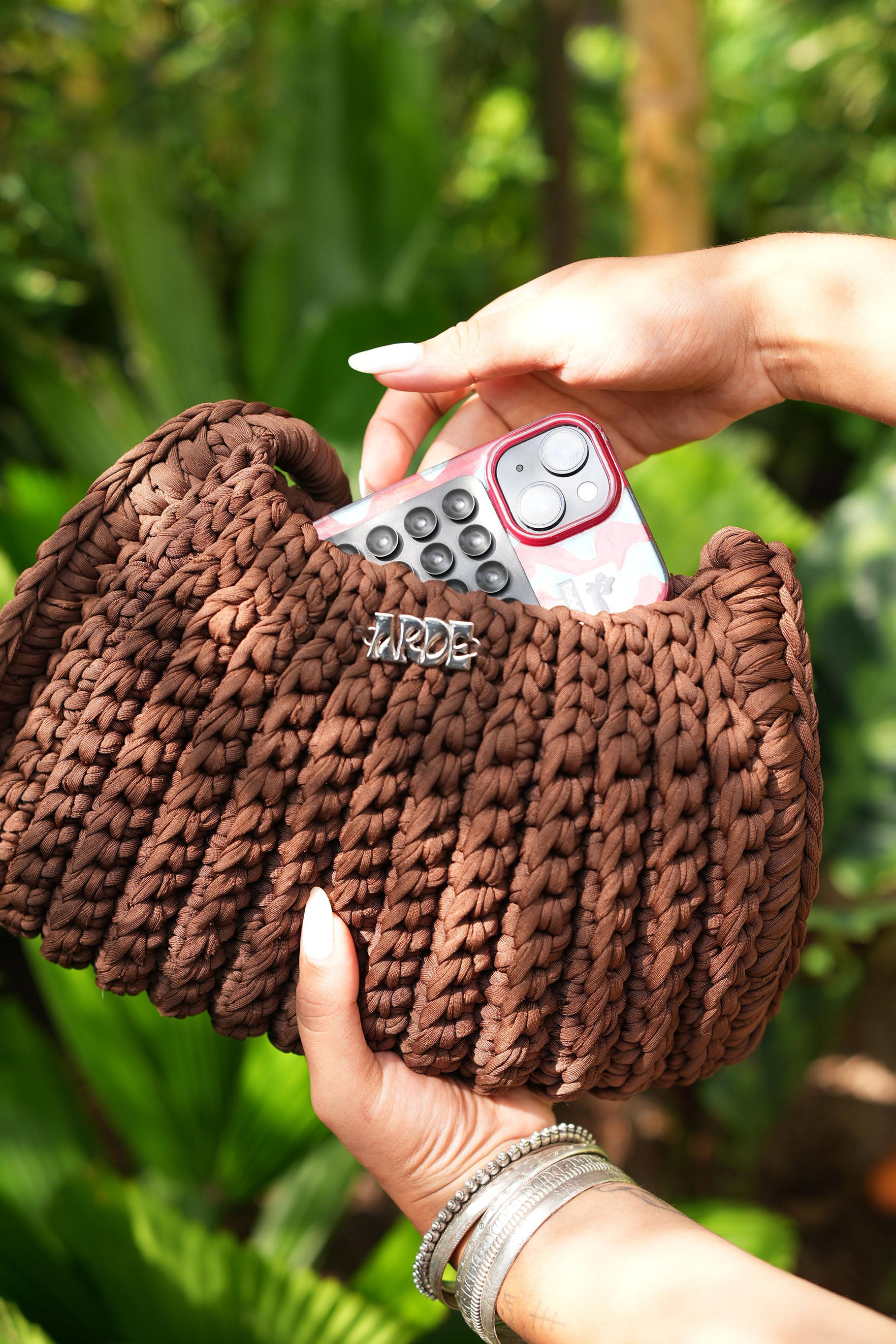 Brown knitted shoulder bag held by a hand with a blurred green background