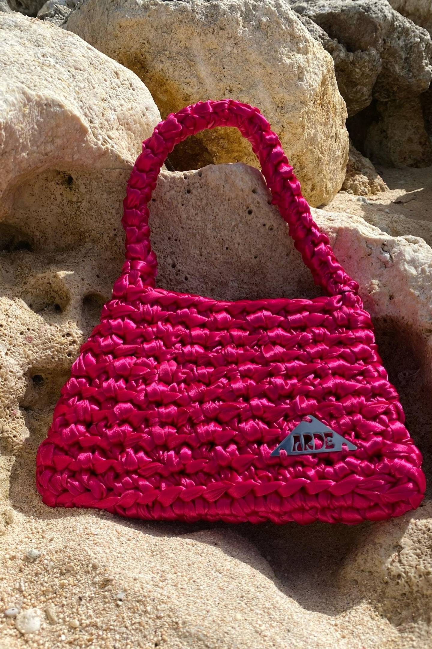 Pink satin ribbon woven handbag with Arde logo on a white rock surface