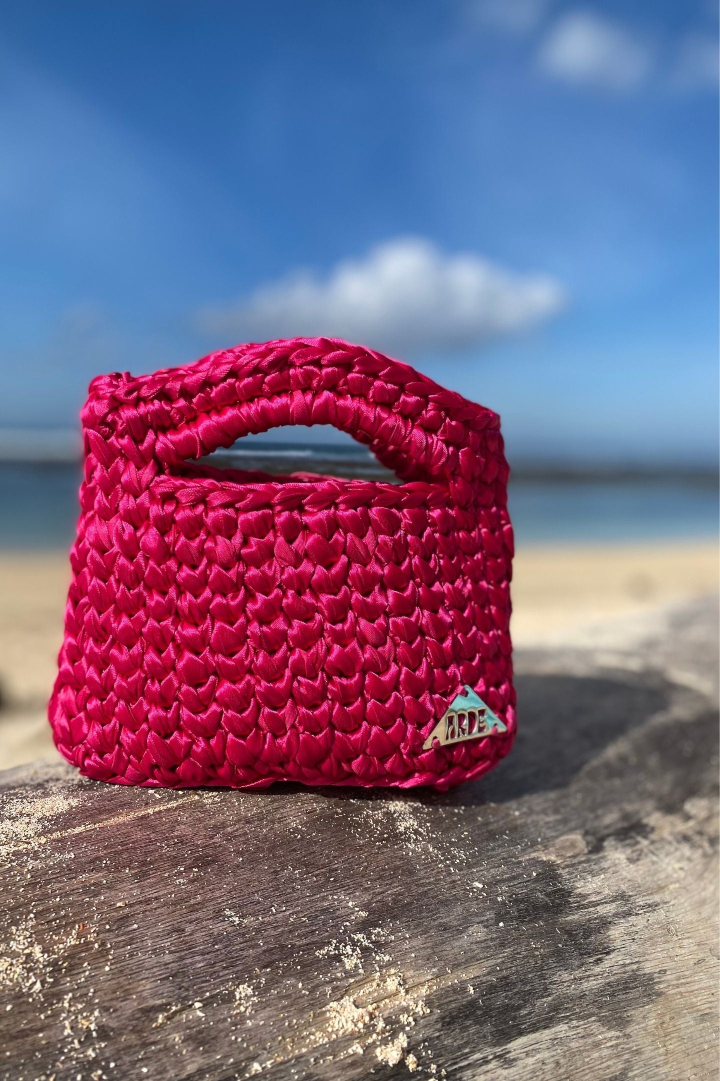 Pink woven handbag on a wooden surface with a beach in the background