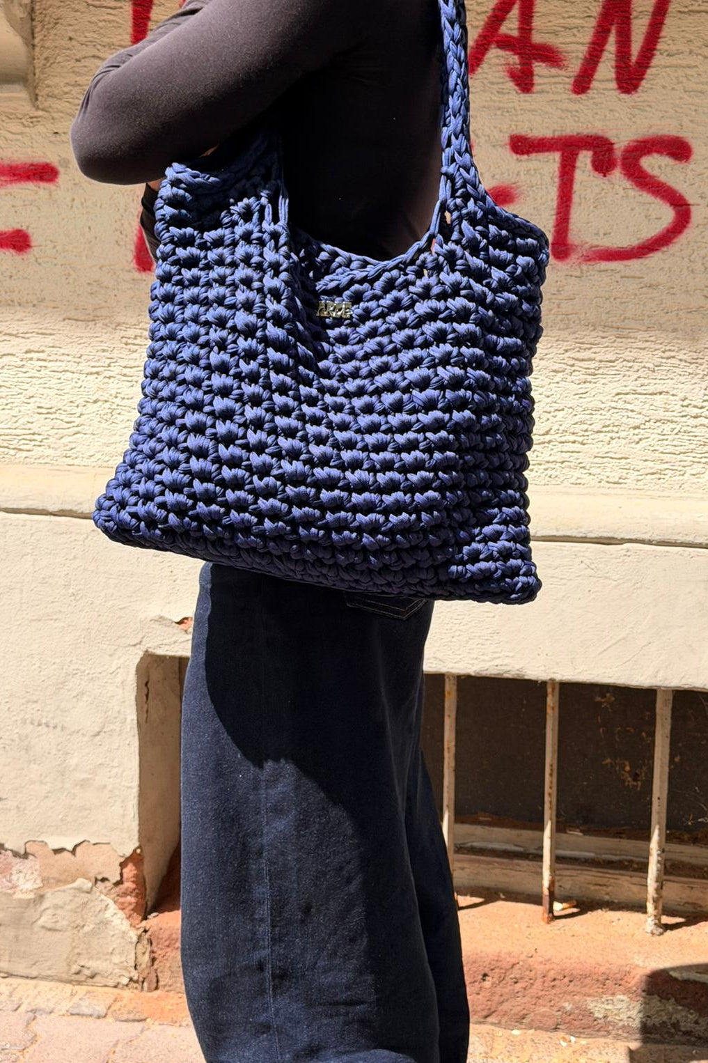 Woman holding a Navy Blue hand-crocheted bag against a graffiti-covered wall.