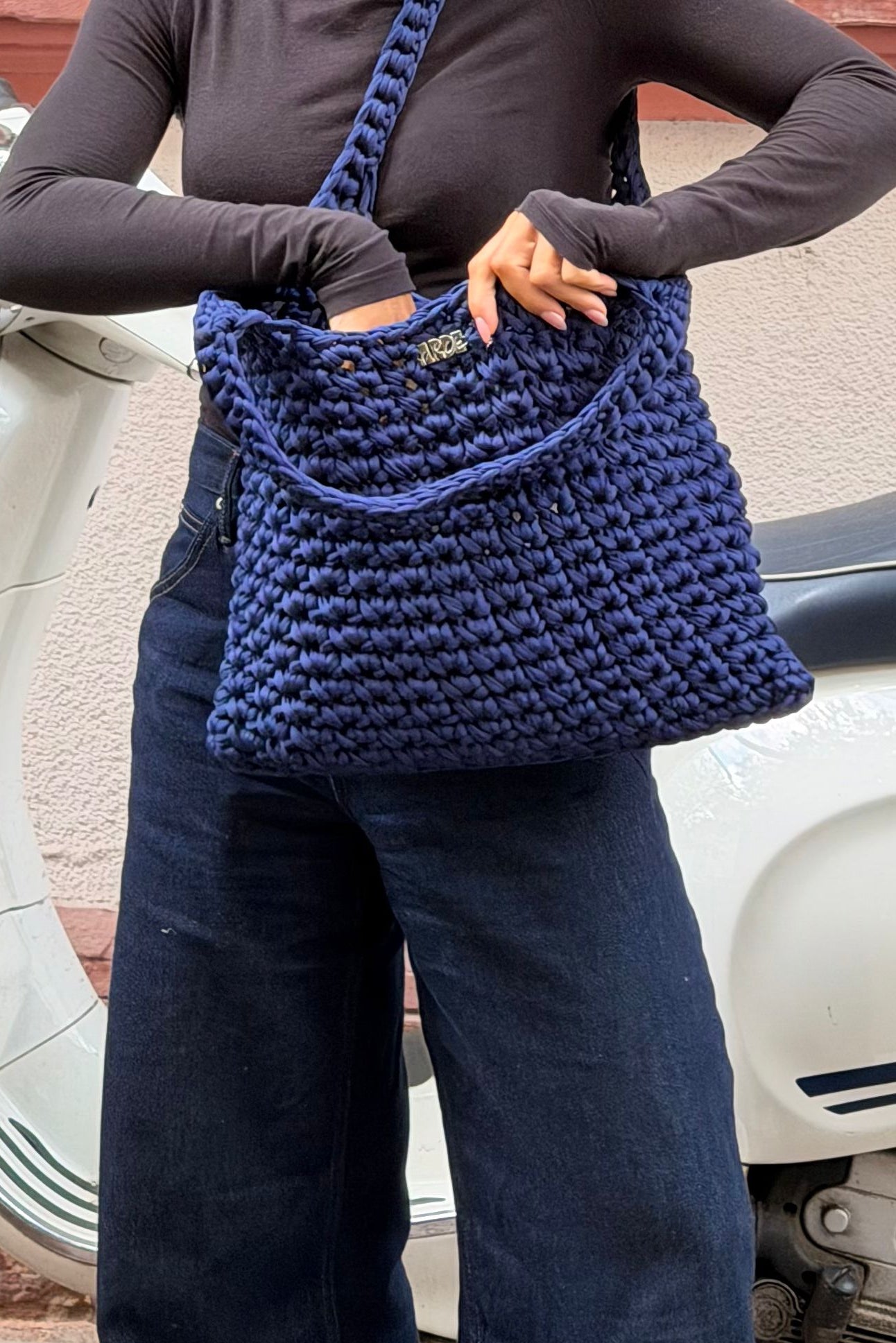 Kenza holding a Blue Crocheted tote bag in front of a Vespa scooter Motorbike