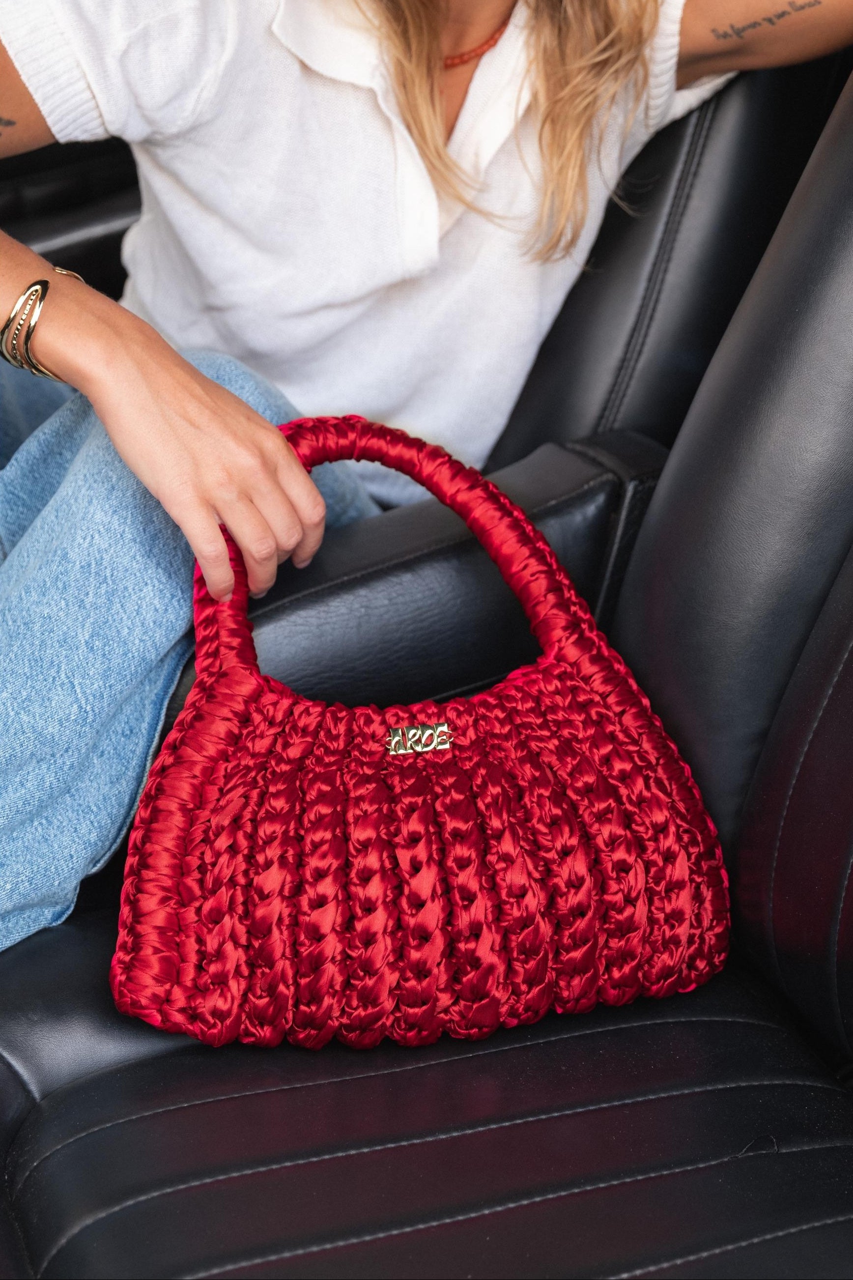 Red knitted handbag held by a elegant dressed woman sitting in a car.