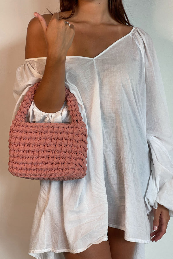 Woman In White Beach Outfit With A Blush Bag
